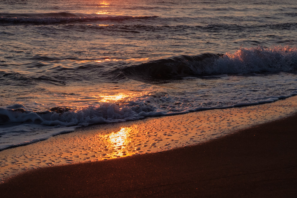 The sun sets over the water and casts an orange glow over the waves